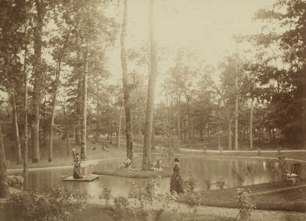 Several adults, two children and a dog enjoying a pond at Bracken Brae, the country home of John Johnston (1836-1904), a successful Milwaukee banker. Hilda Johnston (1883-1974) and Jack Johnston (1884-1939), his two children, are on the island with their dog. Their mother, Ethelinda (Thorsen) Johnston (1856-1947), is in the foreground. Emma Thorsen (1862-1944), sister of Ethelinda, is standing on the raft floating in the pond. Two men are on the far bank.

