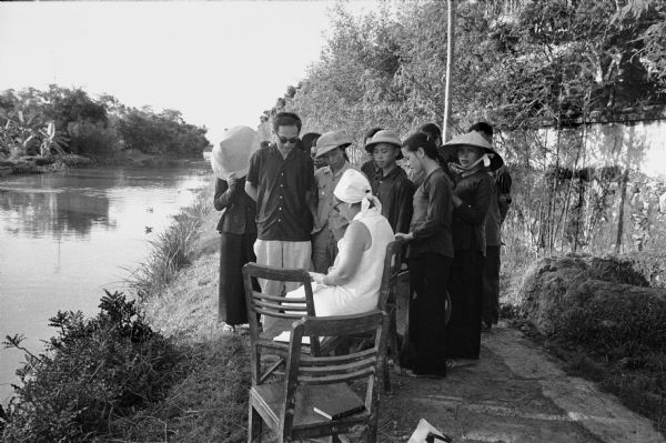 Villagers near Phat Diem gathered to watch American Dorothy Schoenbrun sketching near an irrigation canal. Mrs. Schoenbrun was accompanying her husband, journalist David Schoenbrun, on a two-week tour of North Vietnam.
