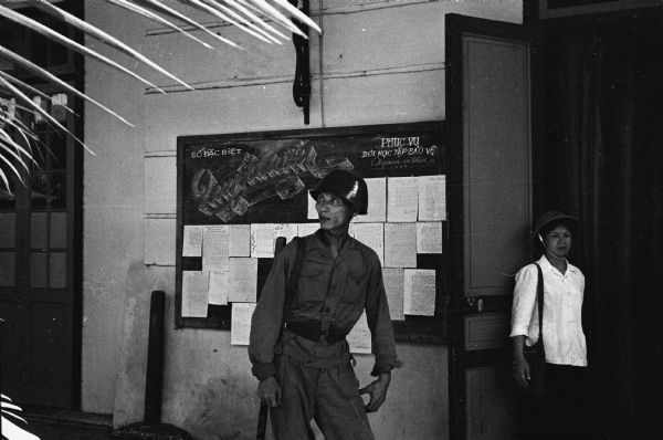 North Vietnamese militia on guard at the door of the Hanoi hotel where American journalist David Schoenbrun was staying. A woman stands in the doorway on the right.
