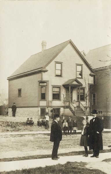 Emil Seidel (left) stands in front of his house with a young girl and another man. Other adults and children are in the background across the street. He was the first Socialist Mayor of Milwaukee.