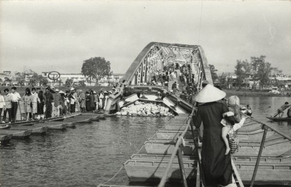 Pedestrians file single file across the make-shift repairs to the bridge over the Perfume River at Hue. The bridge was bombed by the Vietcong during the Tet offensive. This scene was witnessed by American journalist Robert Shaplen.