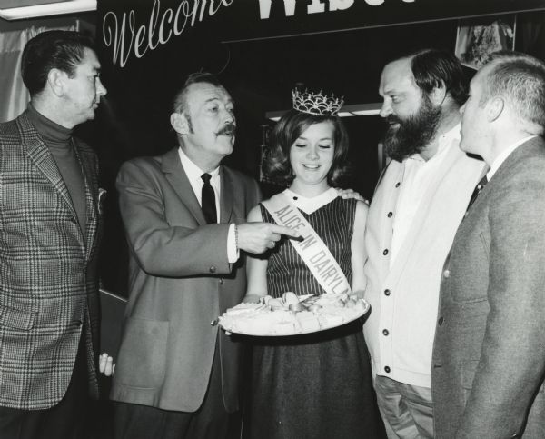 Alice in Dairyland, Bobbie Thoreson, holding a platter of cheese, poses with four men at the World Food Expo.