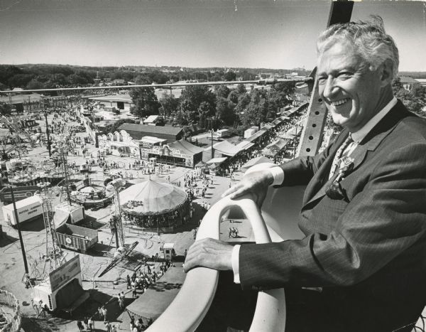 A smiling Governor Knowles surveys the Wisconsin State Fairground from the top of the giant Ferris Wheel on the fair's midway. He spent the day at the State Fair and was on hand for the first annual Governor's Own Pageant of Drums and Bugles competition.