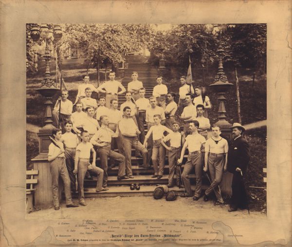 Twenty-seven young men and George Brosius posing outdoors with sporting equipment. The young men are dressed in short sleeved shirts and pants (possibly an athletic uniform), Mr. Brosius wears a suit. This group was the "Milwaukee Herold Team" of the Milwaukee Turners. The photograph was taken to commemorate the 25th Anniversary of the "Milwaukee Herold" and dedicated to the Founder, W.W. Coleman. George Brosius was a gymnastics teacher associated with the Milwaukee Turners from 1854 to 1915.