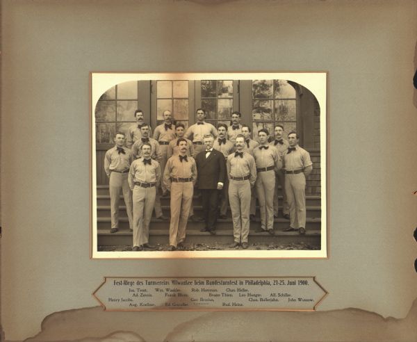 Milwaukee Turners squad at the Federal Gymnastics Festival in Philadelphia. They are dressed in their uniforms and George Brosius is wearing a suit. They are posing outdoors on the steps of a building. George Brosius was a gymnastics teacher associated with the Milwaukee Turners from 1854 to 1915.