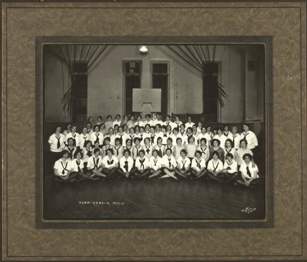 Group portrait of women gymnasts from the Milwaukee Turners in a gymnasium. They are wearing uniforms with middy blouses.