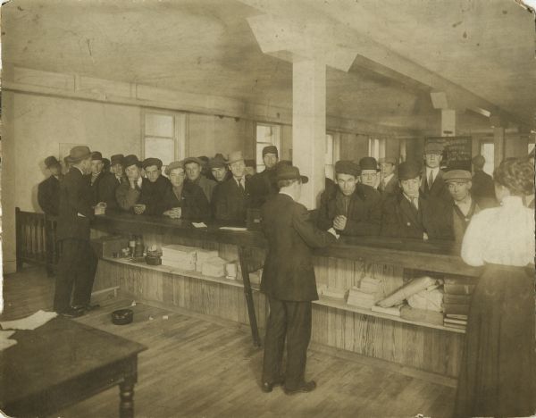 View from behind the counter of men lined up in the Second Office of the State Employment Agency. Three people in the foreground are providing assistance, two men and one woman.