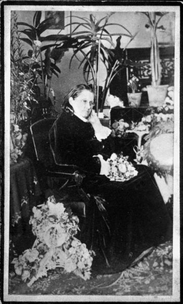 Portrait of Mathilde Franziska Anneke seated, surrounded by flowers and plants.