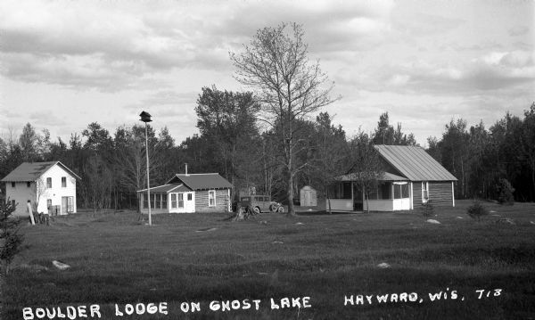 A car parked by resort cabins on cutover land. There is a birdhouse perched on a tall pole in the yard.