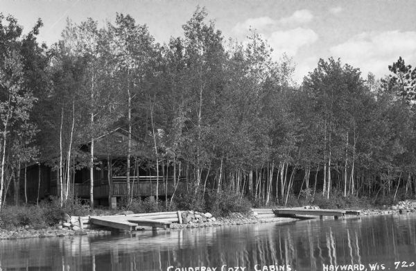 View from water of northern Wisconsin cabin in the woods with boat docks along the rip-rapped shore.