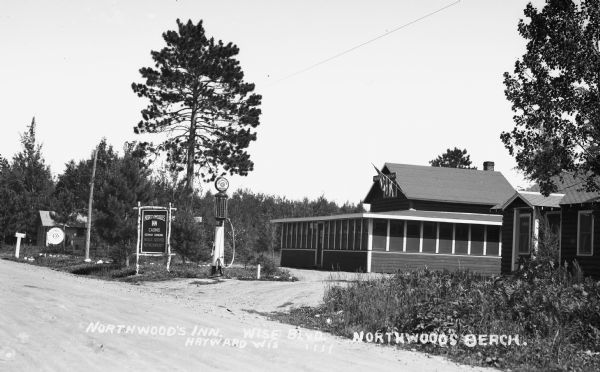 View from road of clapboard buildings, one with a large enclosed front porch, bordering the roadway. There is a Cities Service Oils gas pump and a sign for "Northwoods Inn".