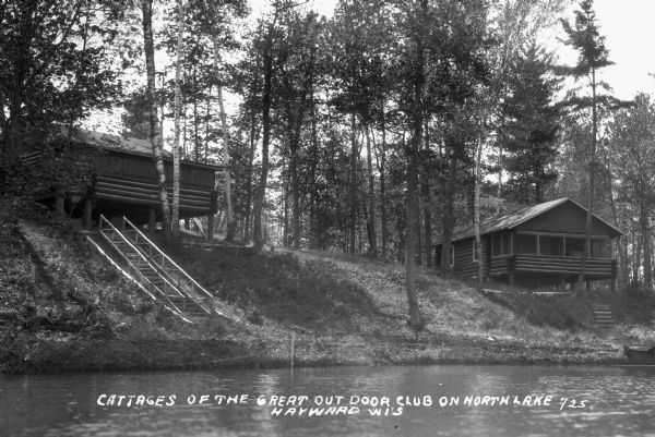 View from North Lake of log cabins on top of low hill. A wooden set of stairs with a railing leads down to the shoreline.