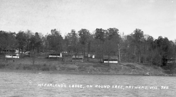 View from lake of numerous cottages and outhouses on hillside near Round Lake.