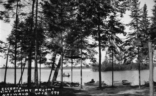 View from lawn of two men in a wooden rowboat on Spider Lake. There are two docks each with a wooden rowboat tied to it.