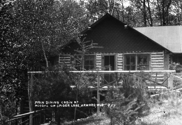 Exterior view of log building with a rustic deck and two small birdhouses attached under the eaves. The building is situated in a forest setting.