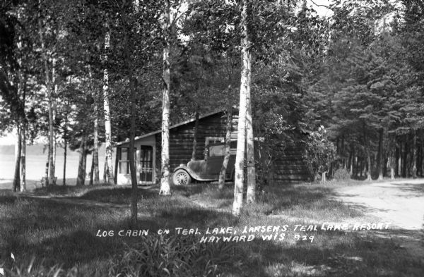 Automobile parked next to log cabin situated near shore of Teal Lake.