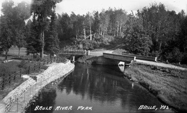 Elevated view of the Brule River in northern Wisconsin, flowing between a road and landscaped stone wall under a bridge and pedestrian walkway.