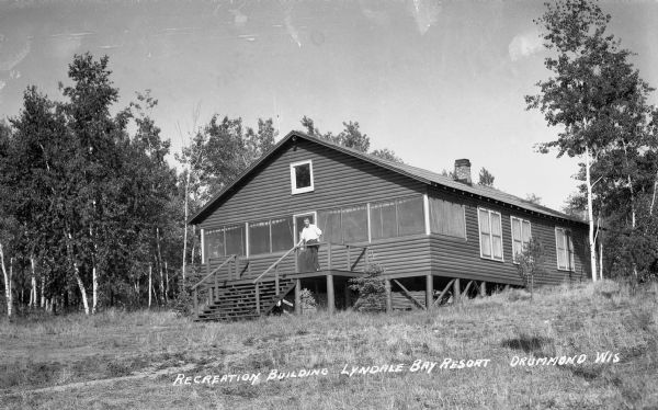 Man standing on the porch of a log building at Lyndale Bay Resort on Upper Eau Claire Lake.