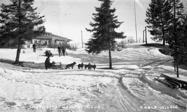Winter scene with people sledding, dog sledding, snowshoeing, and preparing for snowshoeing at Lakewood Country Club.