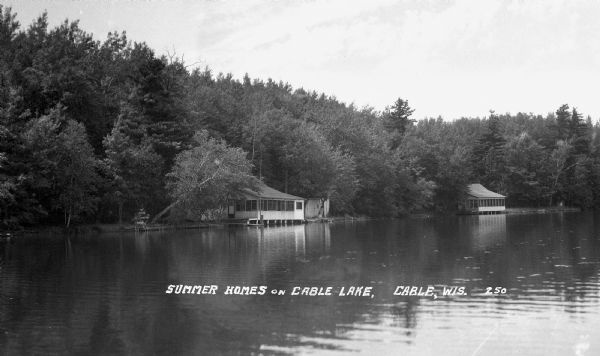 Cottages on the shoreline of Cable Lake. The cottages are supported by pilings where they extend out over the water.