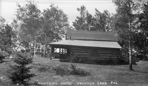 Log cabin with a porch in a clearing of young trees close to the shore of Jackson Lake.
