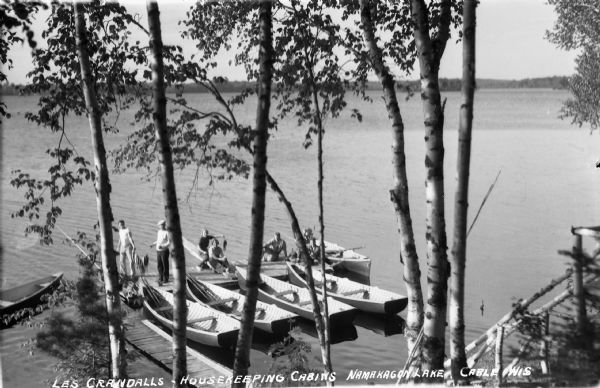 Elevated view of people on boat dock on Namakagon Lake. Some of them are holding stringers of recently caught fish, and wooden rowboats are tied to the dock.