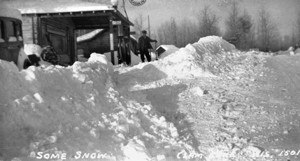 Winter scene with snow piled high in front of Red Crown gasoline station. A man is standing next to the Red Crown gas pump.