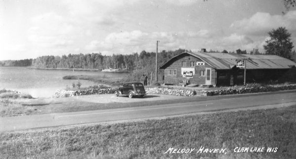 Elevated view of Melody Haven Tavern near Clam Lake. A man is standing next to a stone wall surrounding a parking lot.   
