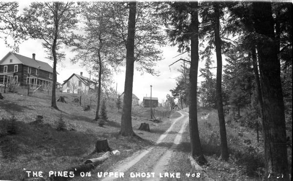 Automobile ruts leading through trees past dwellings on a hill.