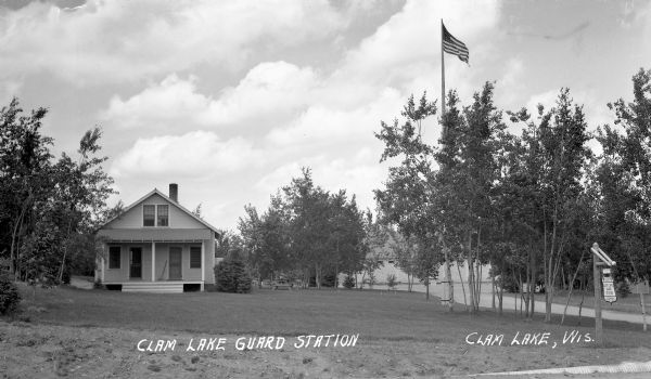 View across lawn of Chequamegon National Forest Guard Station sign in front of one-story guard station building with two front doors.
