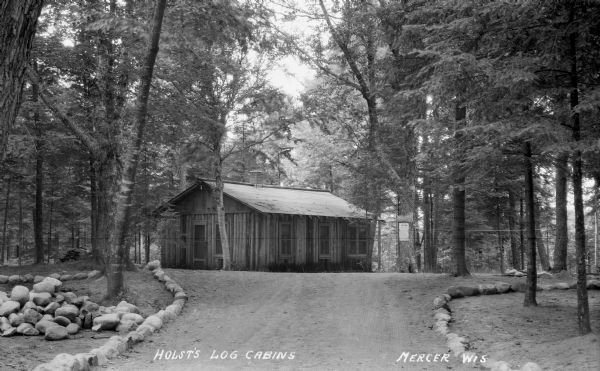 Road lined with stones leading up to the one-story Holst's Log Cabin in the woods.