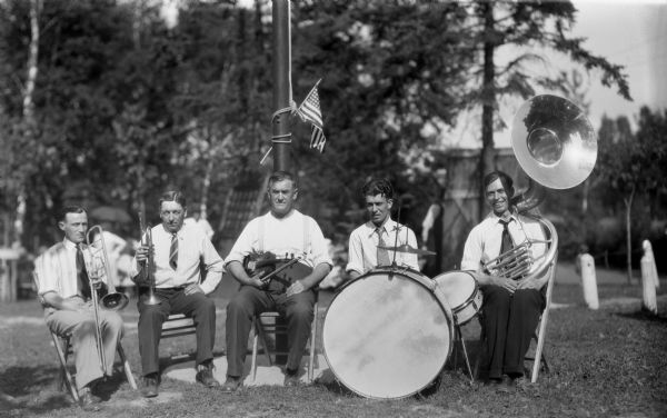 Five band members sitting outdoors holding their instruments.