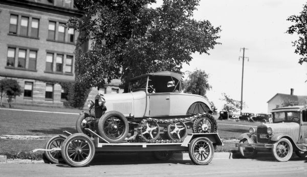 A coupe rag top automobile that has been modified with tracks, sitting atop a trailer in front of the County Courthouse.