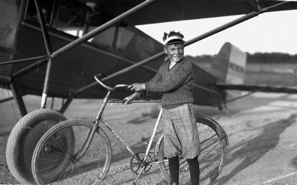 Boy standing next to his bicycle under an airplane wing.
