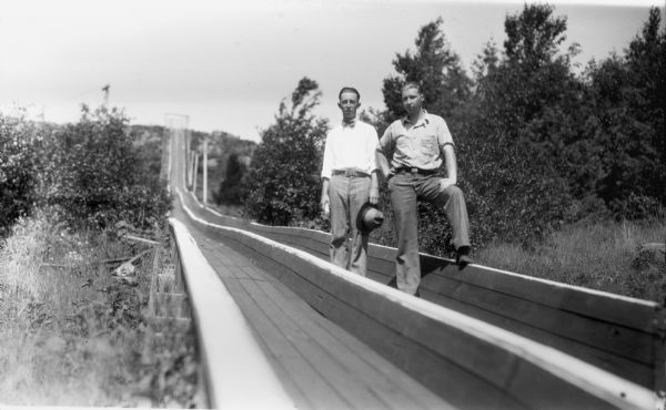 Two men are standing inside a bobsled chute during the summer. The chute is possibly located at the Valhalla ski area in the Chequamegon National Forest.