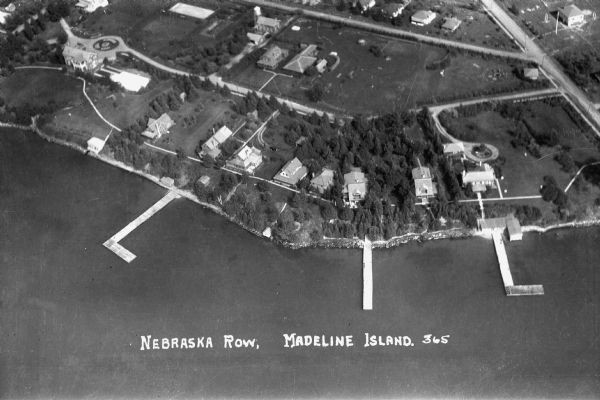 Aerial view of Nebraska Row on the lakeshore of the west side of La Pointe, showing houses, roads and piers. Nebraska Row was started in 1899 when summer resident Col. Frederick Woods built the first house in this area.