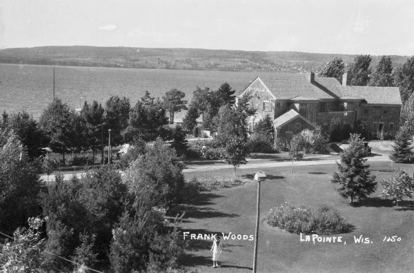 Elevated view of a woman standing on lawn of the Woods mansion on Nebraska Row. Bayfield is visible on the opposite mainland shore of Lake Superior.