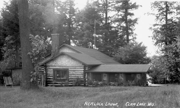 Exterior view of Hemlock Lodge, a one-story log and wood building with a brick chimney. There is a lawn chair on the far left.