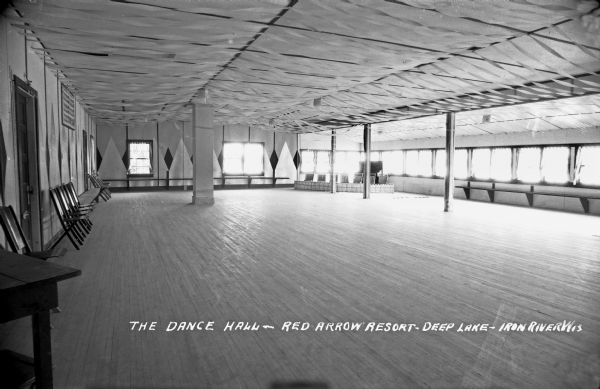 Interior view of the Dance Hall at the Red Arrow Resort on Deep Lake.  There are streamers decorating the ceiling and chairs and benches along the walls.