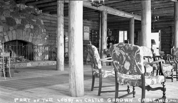 Interior view of part of the lobby at Castle Garden Resort on Lake Namakagon. A large stone fireplace is on the left with elegant chairs on the right. The interior walls, columns and beams are all logs.