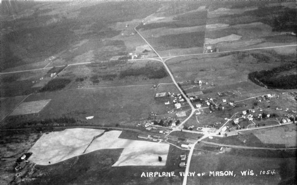 Aerial view taken from an airplane overlooking the town of Mason. Farm fields, roads, trees, houses and other buildings are visible.