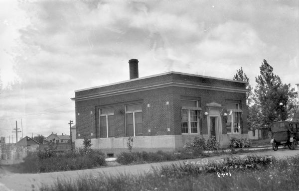 Exterior view of a one-story brick building with a brick chimney, the Mason State Bank. An automobile is parked nearby, and in the background are other buildings.