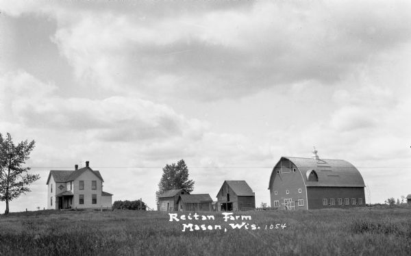 View of the Reitan Farm in showing the two-story farmhouse on the left, a large barn on the right, and three other wood farm storage buildings in the center.