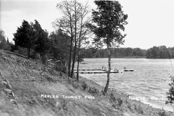 View from the shoreline at Mercer Tourist Park showing people on the dock and floating rafts in the lake.