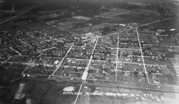 Aerial view, taken from an airplane, overlooking the streets, houses, stores, trees and railroad cars.