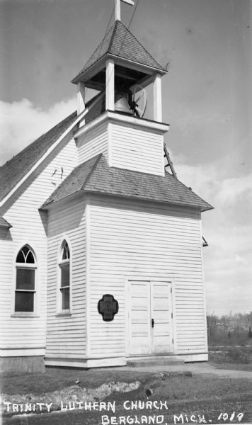 Exterior view of a wooden building showing the front doors, stoop and bell tower of the Trinity Lutheran Church.