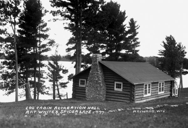 Single-story log cabin with stone fireplace chimney on shore of Spider Lake.