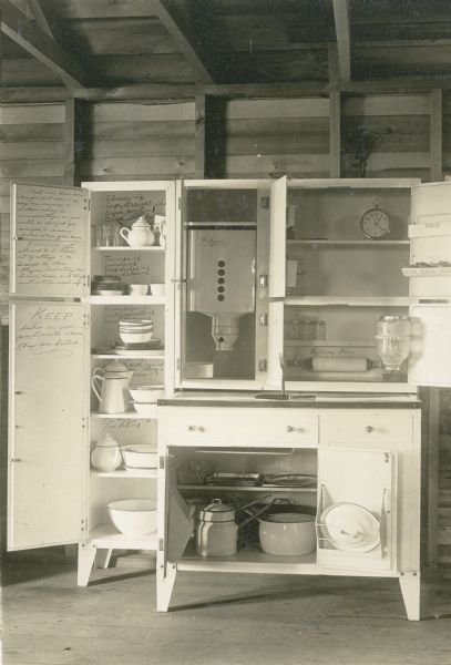 Interior view showing the kitchen setup of a cottage at Nature Lovers Paradise on Jackson Lake near Grand View. Typed description with photograph says, “Study this photo carefully. Every cooking utensil is white enamel, aluminum, or cast iron, whichever is best for the purpose used. White enamel dishes, flour bin, metal lined bread and cake drawers. STAINLESS STEEL cutlery. Porcelain top work table. Porcelain rolling pin. We believe that the ladies can come from the finest of homes; and will find here as good equipment to get meals with than they have at home."<p>Located within the Chequamegon National Forest, Jackson Lake is a 142-acre drainage lake with a navigable outlet channel to Namakagon Lake – which is a 3,227 acre drainage lake at the headwaters of the Namakagon River in Bayfield County.</p>