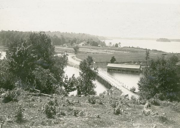 Elevated view overlooking a road leading toward water, a boathouse, cabins, and a lake, most likely Jackson Lake. The shoreline on the far top right is identified as "A small part of our shore." Nature Lovers Paradise was a place to rent cottages on Jackson Lake. Text describing this photograph says, "shows shoreline opposite our cottages.<p>Located within the Chequamegon National Forest, Jackson Lake is a 142-acre drainage lake with a navigable outlet channel to Namakagon Lake – which is a 3,227 acre drainage lake at the headwaters of the Namakagon River in Bayfield County.</p>