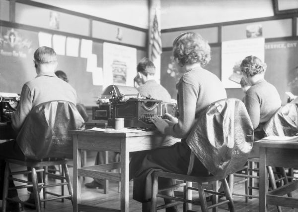 Interior view of a classroom with young men and women learning about, and working on, typewriters.